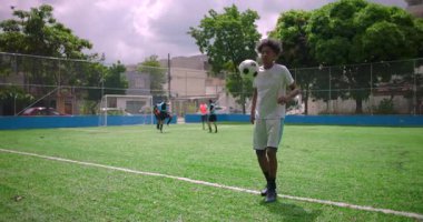 Sıradan bir maç sırasında futbol sahasında tekmeler atan Afrikalı Latin bir adam, takım arkadaşları arkada oynarken futbol topunu ustalıkla dengeliyor.