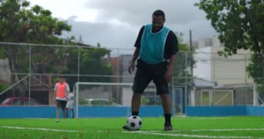 Futbol oyuncusu dışarıda antrenman yaparken sahada top yuvarlama alıştırması yapıyor.