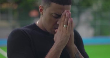 Afrika kökenli bir adam yoğun bir duayla başını eğiyor, elleri sıkıca birbirine kenetlenmiş, dışarıda inanç anında tevazu, güç ve duygusal bağlılık gösteriyor.