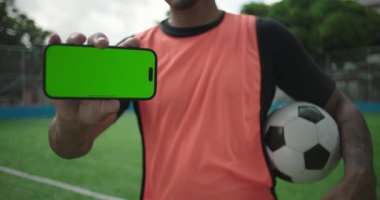 Afrika kökenli, gülümseyen Latin Latin asıllı, futbol sahasında yeşil ekranlı akıllı telefon, mobil uygulama veya sosyal medya için dijital model, aktif yaşam tarzı gösteren,