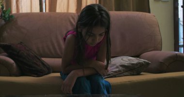 Kız kanepede yatar, kasvetli bir ifadeyle boş boş bakar, depresyon temalarını somutlaştırır, izolasyon ve genç iç gözlem sakin ama melankolik bir ortamda.