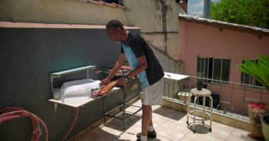 Afro-Amerikalı bir adam, terasta ızgara yaptıktan sonra bir şeyler düzenliyor, rahat bir şehir ortamında çalışma alanı düzenliyor.