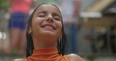 Gülümseyen kız dışarıda sudan zevk alıyor, başı arkaya eğik, gözleri kapalı, neşe ve rahatlama saçan, neşeli ve ferahlatıcı bir yaz anını canlı bir enerjiyle yakalıyor.