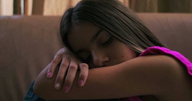 Genç kızın başını kollarının üzerinde dinlendirme, üzüntü, yalnızlık ve içgözlem, çocukluk depresyonu ve duygusal izolasyon temalarını vurgulama.