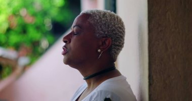 Derin düşüncelere sahip bir kadın, kapalı gözlerle duvara karşı duruyor, duygusal ifade, açık hava düzeni, yakın plan, Afrika kökenli, pişmanlık, sıkıntı, duygusal karmaşa