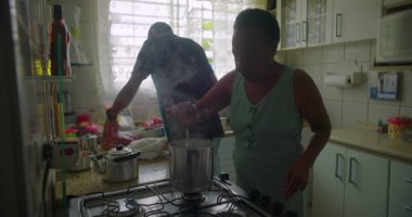 Afrikalı bir kadın mutfakta yemek pişiriyor, sobanın yanında yemek hazırlıyor, buhar yükseliyor, günlük hayatı, yemek hazırlıklarını ve aile anlarını gözler önüne seriyor.