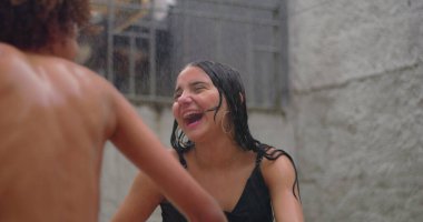 Gençler gülüyor ve yağmurdan zevk alıyorlar, saf neşe ve bağlantı anında el ele tutuşuyorlar, gençlik enerjilerini ve çeşitli arkadaşlıkları sergiliyorlar.