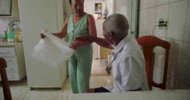 Yaşlı Afrikalı Amerikalı çift, sıcak bir mutfak ortamında şefkatli bir öpücük paylaşıyor, sevgi ve bağlantı sergiliyorlar, evcil bir atmosferle.