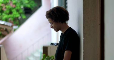 Genç bir çocuk gülümsüyor ve konuşuyor, anlamlı bir an, duvara yaslanmış, Afrika kökenli, açık hava, neşeli bir ifade, vücut dili