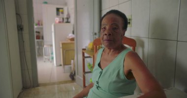 Rahat bir ev mutfağında yemek masasında oturan yaşlı Afro-Amerikalı kadın, hafif bir kızgınlıkla iç çekiyor, yalnızlığı ve duygusal derinliği yansıtıyor.