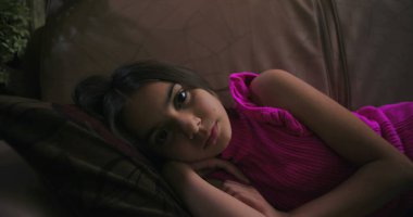 Uzak bir bakışla kanepede uzanan genç kız, sakin, ev ortamında yalnızlık, üzüntü ve çocukluk duygularını ifade ediyor.