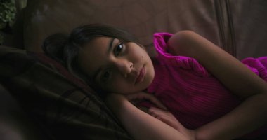 Uzak bir bakışla kanepede uzanan genç kız, sakin, ev ortamında yalnızlık, üzüntü ve çocukluk duygularını ifade ediyor.