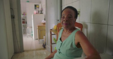 Rahat bir ev mutfağında yemek masasında oturan, düşünceli, bilgeliği ve yalnızlığı yansıtan yaşlı Afrikalı Amerikalı kadın, her gün huzurlu bir ortamda.