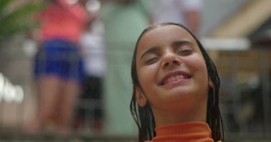 Gülümseyen kız dışarıda sudan zevk alıyor, başı arkaya eğik, gözleri kapalı, neşe ve rahatlama saçan, neşeli ve ferahlatıcı bir yaz anını canlı bir enerjiyle yakalıyor.