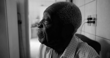 Siyah-beyaz görünümlü yaşlı bir Afro-torunu, düşünceli ve sakin bir ifadeyle yukarı bakıyor, sessiz bir ev ortamında oturuyor