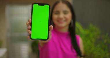 Genç kız gülümsüyor ve elinde yeşil ekran ve krom anahtarı olan akıllı telefonu tutuyor. Canlı bir açık hava ortamında kişiselleştirilebilir bir cihaz sergiliyor.