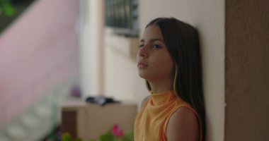 Duvara yaslanan genç bir kız, uzaklığa dalgın dalgın bakıyor, iç gözlem, sakinlik ve dış mekânda sessizce tefekkür temaları yansıtıyor.