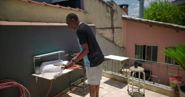 Afro-Amerikalı bir adam, terasta ızgara yaptıktan sonra bir şeyler düzenliyor, rahat bir şehir ortamında çalışma alanı düzenliyor.