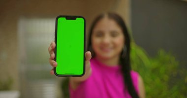 Genç kız gülümsüyor ve elinde yeşil ekran ve krom anahtarı olan akıllı telefonu tutuyor. Canlı bir açık hava ortamında kişiselleştirilebilir bir cihaz sergiliyor.