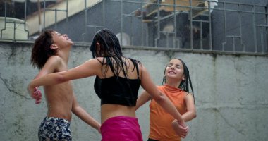 Çeşitli etnik kökenlere sahip gençler yağmurun tadını çıkarıyorlar, açık havada eğlenceli bir anda el ele tutuşuyorlar, neşeli ve kaygısız bir birlik ve dostluk ortamı yaratıyorlar.