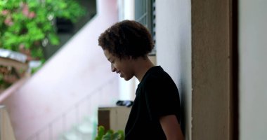 Genç bir çocuk gülümsüyor ve konuşuyor, anlamlı bir an, duvara yaslanmış, Afrika kökenli, açık hava, neşeli bir ifade, vücut dili