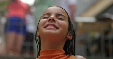 Gülümseyen kız dışarıda sudan zevk alıyor, başı arkaya eğik, gözleri kapalı, neşe ve rahatlama saçan, neşeli ve ferahlatıcı bir yaz anını canlı bir enerjiyle yakalıyor.