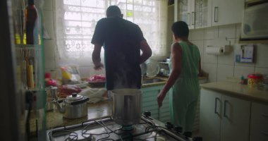 Afrikalı bir kadın mutfakta yemek pişiriyor, sobanın yanında yemek hazırlıyor, buhar yükseliyor, günlük hayatı, yemek hazırlıklarını ve aile anlarını gözler önüne seriyor.