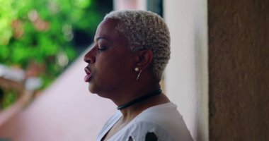 Derin düşüncelere sahip bir kadın, kapalı gözlerle duvara karşı duruyor, duygusal ifade, açık hava düzeni, yakın plan, Afrika kökenli, pişmanlık, sıkıntı, duygusal karmaşa