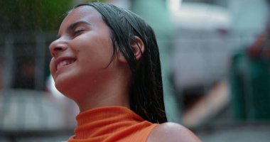 Suyun tadını çıkaran gülümseyen çocuk dışarıda, yüzü eğilmiş, gözleri kapalı, neşe saçan, sükunet ve neşeli, kaygısız bir ortamda doğayla bağlantı kuran çocuk.