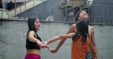 Çeşitli etnik kökenlere sahip gençler yağmurun tadını çıkarıyorlar, açık havada eğlenceli bir anda el ele tutuşuyorlar, neşeli ve kaygısız bir birlik ve dostluk ortamı yaratıyorlar.