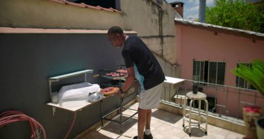 Afro-Amerikalı bir adam, terasta ızgara yaptıktan sonra bir şeyler düzenliyor, rahat bir şehir ortamında çalışma alanı düzenliyor.