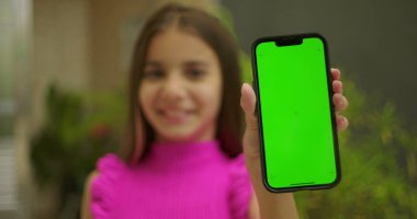 Elinde yeşil ekran ve krom anahtarı olan akıllı telefonu tutan genç bir kız. Kameraya yakın gülümsüyor ve dış mekanda kişiselleştirilebilir görüntüler sergiliyor.