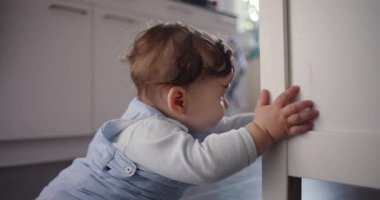 Bebek mutfak dolabına dokunmak için uzanırken yerde oturuyor, erken öğrenme ve duyusal gelişim süresince dokuyu ve uzayı merakla keşfediyor.