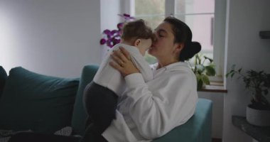 Anne bebeği şefkatle öpüyor, sıcak bir yuva ortamında ona sarılıyor, şefkat ve sevgi gösteriyor.