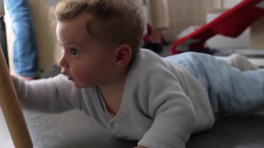 Bebek yerde yatıyor, tahtadan tabureye uzanırken hafifçe yere düşüyor, aile mutfağında erken gelişim, merak ve motor keşifleri gösteriyor.