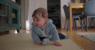 Bebek yerde otururken rahat bir duruş ve kurnaz bir gülümsemeyle, farkındalık, rahatlık ve erken iletişim ipuçlarıyla yana dönüyor.