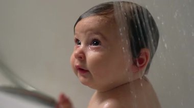 Bebek küvette su yüzüne akarken, masum bebek banyosu zamanı merak ve merakla, sıcak banyo ortamında temiz ve hassas bir çocukluk ifadesi