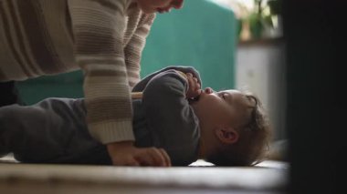 Küçük bir çocuk, bebek kardeşinin üzerine eğiliyor, şefkatle ve merakla bakıyor, sıcaklığını, şefkatini ve aile bağlarını samimi bir şekilde gösteriyor.