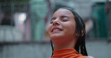 Gözleri kapalı gülümseyen küçük bir kız, canlı bir toplulukta serinletici suyun tadını çıkarıyor, saf neşe yayıyor ve doğayla barışçıl bir bağ kuruyor.