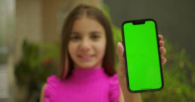 Elinde yeşil ekran ve krom anahtarı olan akıllı telefonu tutan genç bir kız. Kameraya yakın gülümsüyor ve dış mekanda kişiselleştirilebilir görüntüler sergiliyor.