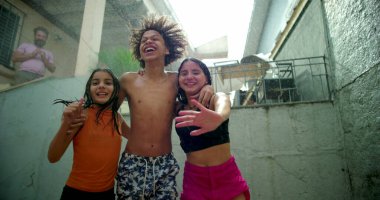 Çocuklar arka bahçede toplanırken suda gülüp oynuyorlar, el ele tutuşuyorlar ve açık havada kaygısız ve neşeli bir anın tadını çıkarıyorlar.