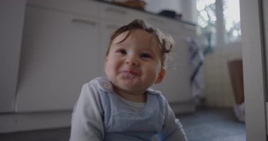 Bebek mutfak zemininde oturmuş tatlı tatlı gülümsüyor, erken gelişim süresince masumiyetin ve sıcaklığın neşeli ifadesi ve aile ortamında neşeli bir keşif.