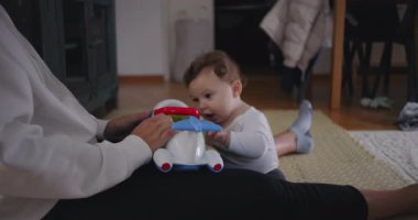Bebek annesinin yanında oturuyor, sıcak aile ortamında koordinasyon ve merakı öğrenirken renkli oyuncak uçakla oynuyor.