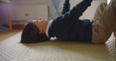 Çocuk yerde yatıp altın balonla oynuyor, hayal gücünü ve konsantrasyonunu kapalı oyun saatinde gösteriyor.