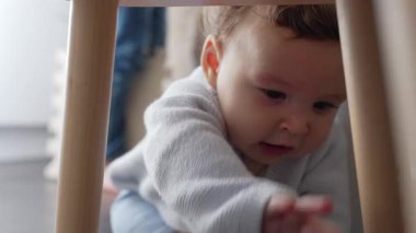 Bebek evdeki ahşap taburede oturuyor, merak ve keşif anında elini uzatıyor, güvenli aile ortamını keşfediyor.