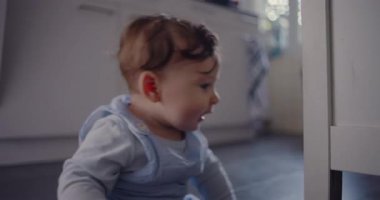Bebek mutfak zemininde otururken tuhaf bir ifadeyle başını çeviriyor, çevreyi gözlemliyor ve gelişim aşamasında erken keşiflere girişiyor.