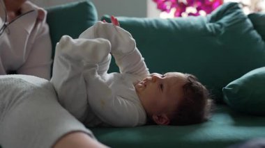Sevimli bebek kanepede yatıyor, annesi yakınlarda oturuyor.