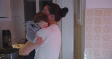 Anne, mutfakta bebek beşiği, tencere tavalar, ebeveynlik kavramı, aile hayatı ve koşulsuz sevgi ile çevrili.