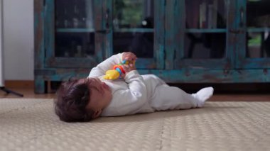 Bebek yerde yatıp oyuncakla oynuyor..