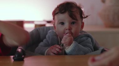 Bebek sandalyeye oturmuş, tuhaf bir şekilde masaya bakıyor, sevimli bebek çevreyi incelikli bir ifadeyle keşfediyor, çocukluk kavramı, masumiyet, aile ve keşif kavramı.